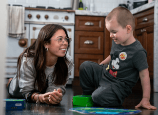 Childcare Stress? Consider Hosting an Au Pair Young woman sits on floor with toddler
