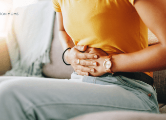This Ovarian Cancer Awareness Month, Remember to Listen to Your Body woman seated on couch holds abdomen in pain