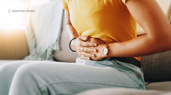 This Ovarian Cancer Awareness Month, Remember to Listen to Your Body woman seated on couch holds abdomen in pain