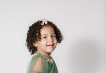 Portrait of toddler smiling with pink bow and curly hair by Danielle West Photography