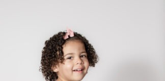 Toddlers and Teens: The Wild, Wonderful Bookends of Childhood Portrait of toddler smiling with pink bow and curly hair by Danielle West Photography