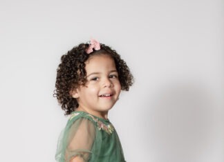 Portrait of toddler smiling with pink bow and curly hair by Danielle West Photography