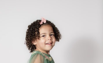 Portrait of toddler smiling with pink bow and curly hair by Danielle West Photography