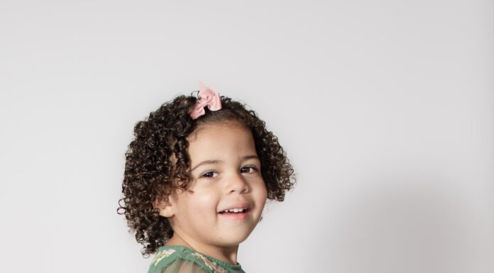 Portrait of toddler smiling with pink bow and curly hair by Danielle West Photography