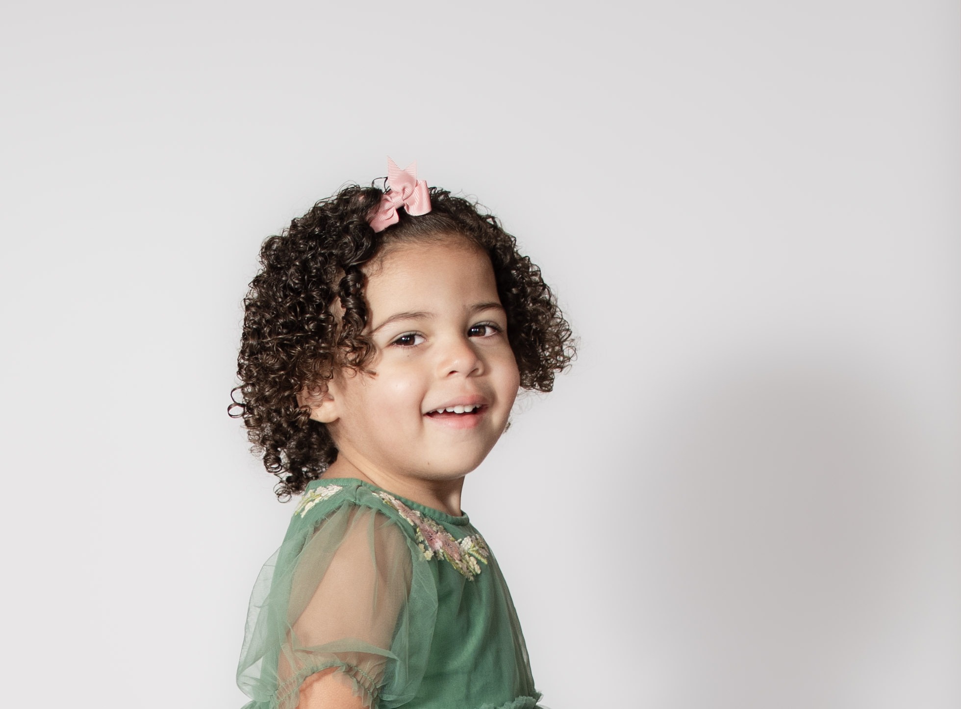 Toddler milestone portrait for birthday by Danielle West Photography Portrait of toddler smiling with pink bow and curly hair by Danielle West Photography