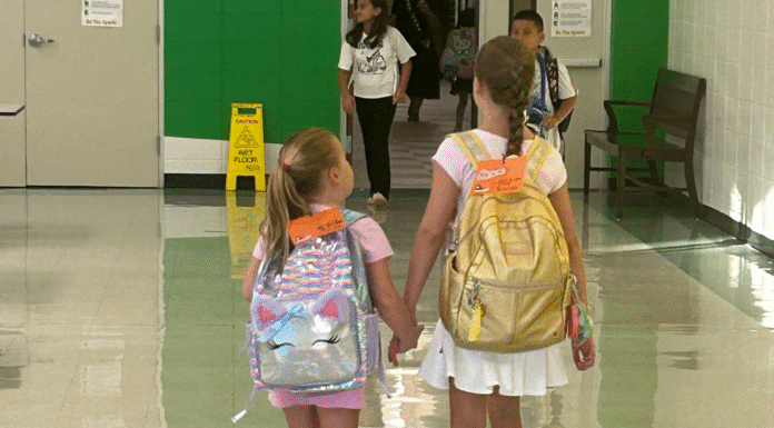 When School Closures Stop Being a Headline and Become Your Child’s School Sugar Mill Elementary, sisters holding hands, walking down hallway