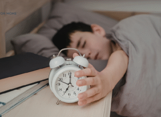 How to Help your Kids Adjust to Daylight Saving Time child in bed reaching for alarm clock