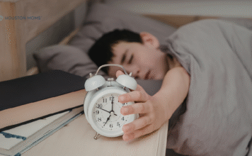 How to Help your Kids Adjust to Daylight Saving Time child in bed reaching for alarm clock