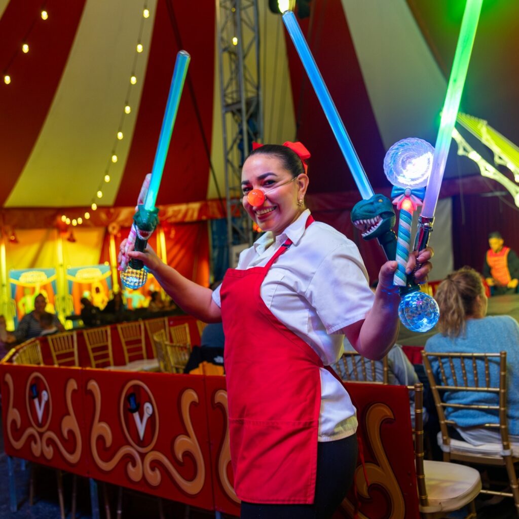 circus performer with red nose holds light up wands