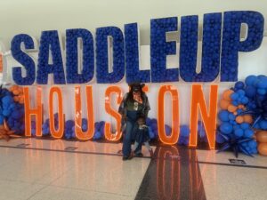 Child poses in front of a Saddleup Houston sign