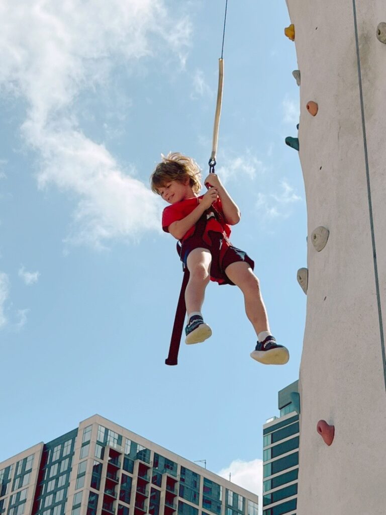 child hangs from rope while rock climbing