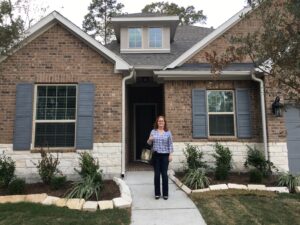 woman holding baby carrier stands in front of home