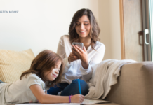 Mom sitting on couch looking at her phone while child draws next to her