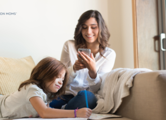 Mom sitting on couch looking at her phone while child draws next to her