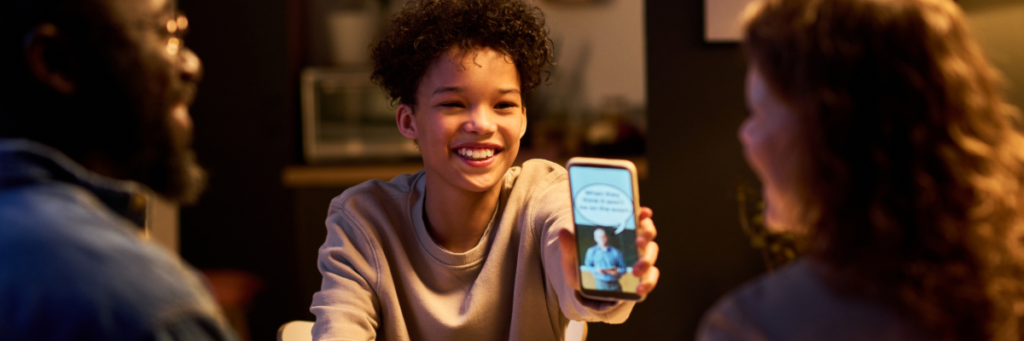 Stock image of teen showing parents a meme at dinner